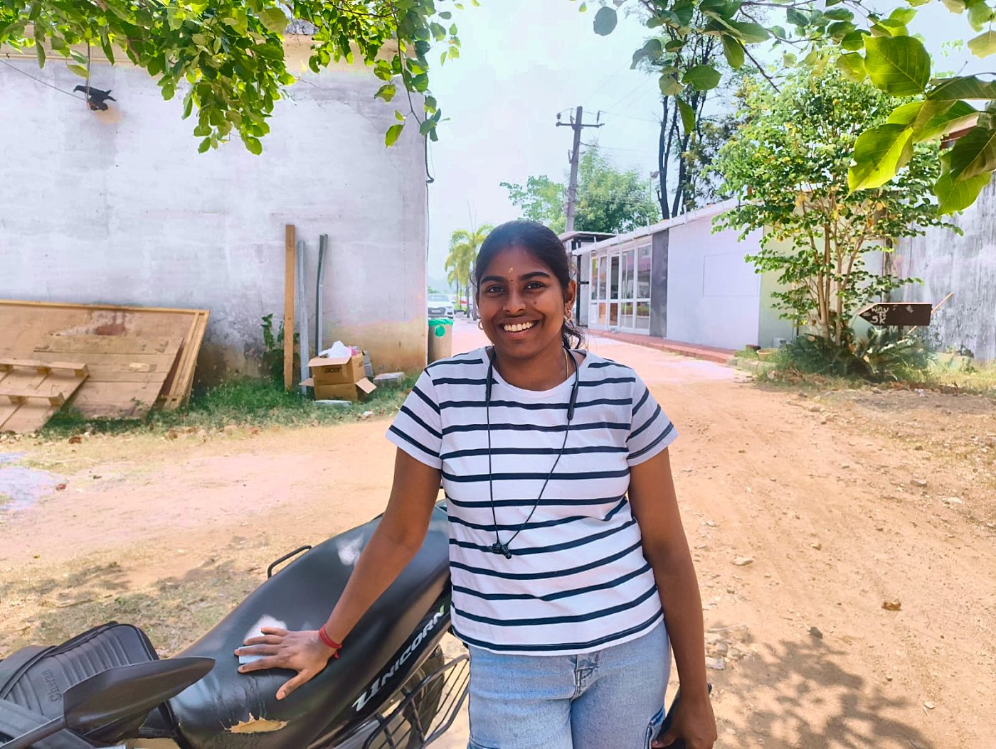 Kaviya leaning on the bike, smiling