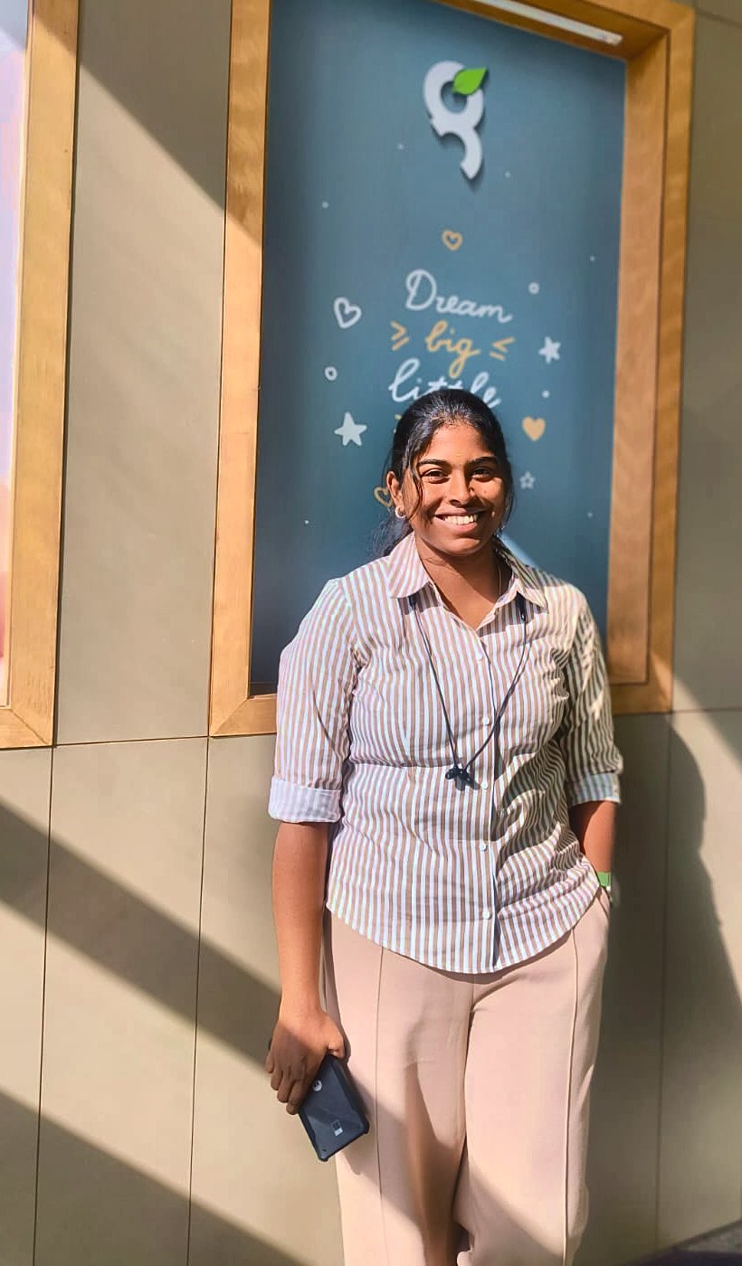 Kaviya smiling in front of a Dream big poster